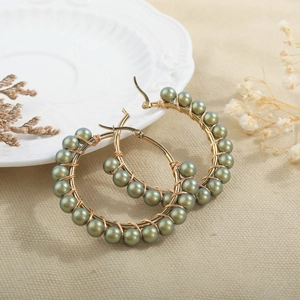 Detail of handmade beaded hoop earrings with gold wire wrapping and olive green pearls