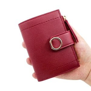 Red leather short wallet for women featuring a gold zip and metal buckle held by hand