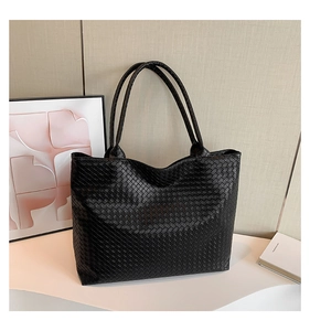 Detailed view of black woven leather tote bag texture on a minimalist display
