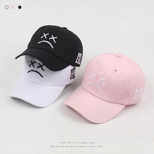 Close-up of stacked baseball caps in black, white, and pink with sad face embroidery