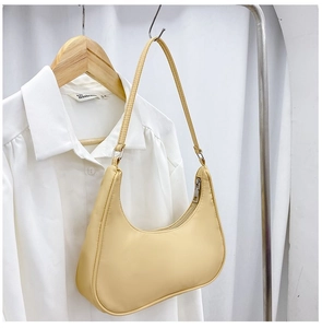 Detailed view of a light yellow nylon crescent shoulder bag hanging next to a shirt