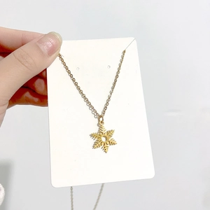 Détail d'un collier pendentif flocon de neige doré tenu sur un fond de carte blanche