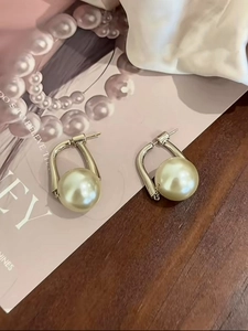 Detail of elegant gold earrings with oversized faux pearls on a vintage wood and pink background