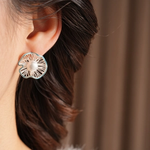 Detailed close-up of a silver floral pearl earring worn on the side of a model's ear