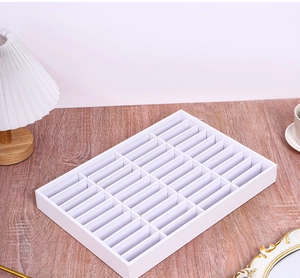 Close-up of a 30-compartment white jewelry display tray for rings and earrings on wood desk
