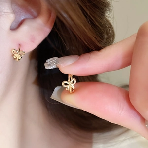 Detailed view of small gold bow-shaped stud earrings worn for an elegant aesthetic