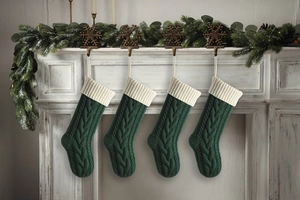 Set of 4 green cable knit Christmas stockings hanging on a festive decorated white mantel