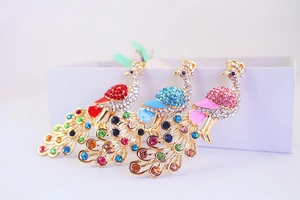 Close-up of three peacock keychains in red, blue and pink with colorful rhinestones