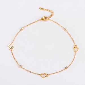 Macro detail of gold-tone hollow heart charm and round zircon pendant on minimalist anklet