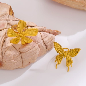Close-up of golden matte flower and butterfly rings on a natural stone surface