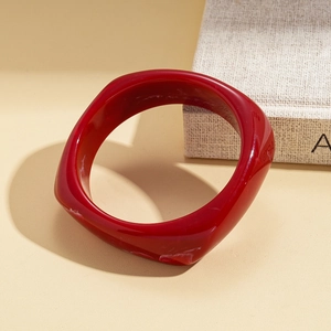 Macro shot of a minimalist deep red resin bangle on warm textured book background