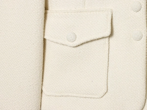 Detailed macro view of off-white tweed texture with a pocket and matching covered button