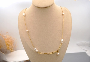 Detail of asymmetrical gold long necklace featuring freshwater pearls on a beige neck bust