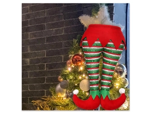 Detail of sequined red and green striped Christmas elf legs hanging on a lighted tree