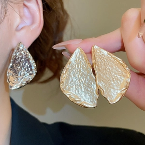 Detail of large hammered metal water drop earrings showing gold and silver wavy texture