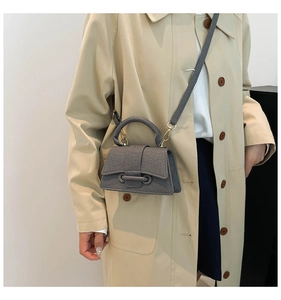 Détail du sac à bandoulière gris avec texture tissée sur un mannequin en trench beige
