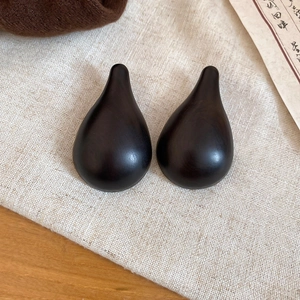 Detailed view of polished ebony wood teardrop earrings resting on beige linen fabric