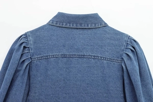 Detail view of denim shirt collar and puff sleeve stitching on blue fabric background