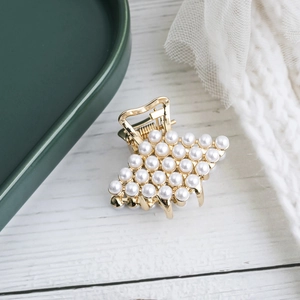 Elegant gold metal hair claw clip with white pearls on white wooden surface