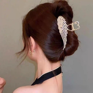 Detailed view of a golden angel wing hair claw with rhinestones on a bun hairstyle