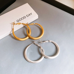 Detail of matte gold and silver large hoop earrings with brushed finish on dark background