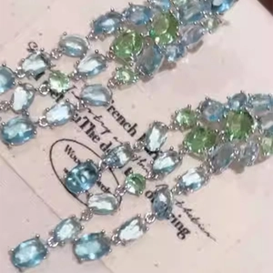 Detail of silver drop earrings with light blue and green oval stones on vintage paper