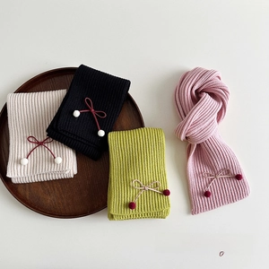Flat lay of knit bow scarves in pink, green, black and beige with soft pompom details
