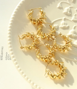 Detailed view of golden twisted croissant hoop earrings on a decorative plate