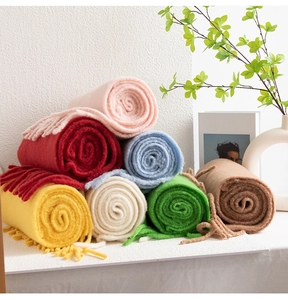Close-up of neatly rolled colorful wool scarves with fringe on a minimalist shelf