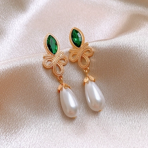 Detail of vintage gold earrings with green marquise stones and drop pearls on silk