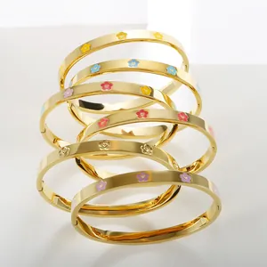 Detail view of stacked gold bracelets featuring colorful enamel floral charms and patterns