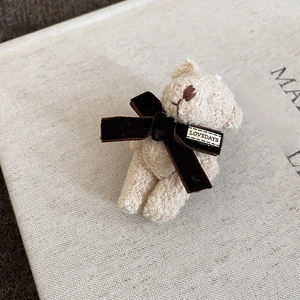 Detailed close-up of a cream velvet teddy bear brooch with soft flocking texture and bow