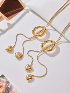 Detailed macro view of long gold tassel necklace with heart pendant and irregular rings