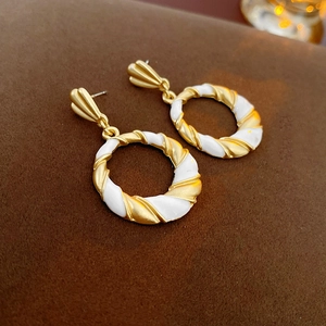 Detail of twisted gold metal hoop earrings with white enamel on dark velvet background