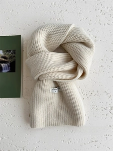 Dettaglio della sciarpa in maglia di lana bianco crema con etichetta su sfondo minimalista