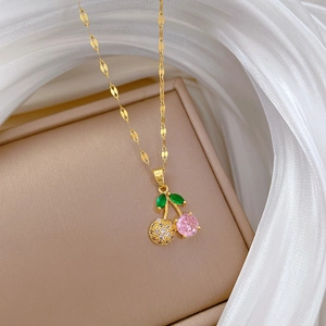 Macro detail of gold cherry pendant necklace with pink crystal and green leaves on silk