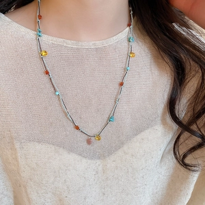 Detail of colorful beads on braided rope necklace worn over a white knit sweater