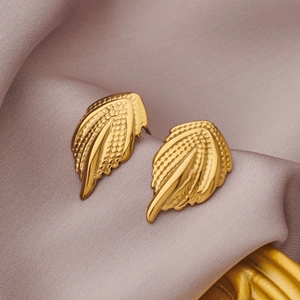 Macro detail of gold-plated wing earrings with fine grain texture on purple silk