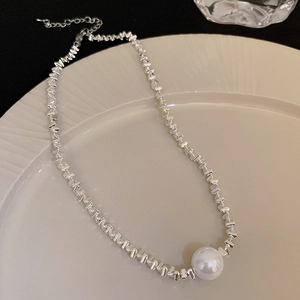 Detail of silver geometric chain necklace featuring a glossy round white pearl pendant