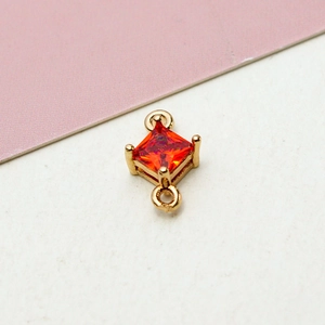 Detailed macro view of a gold plated geometric rhombus pendant with a red zircon stone
