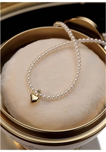 Detailed macro view of white baby pearls and a golden heart pendant on a soft cushion