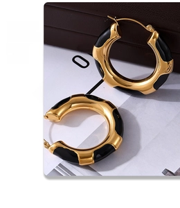 Macro shot of wavy gold-plated hoop earrings with elegant black enamel finish and polished texture