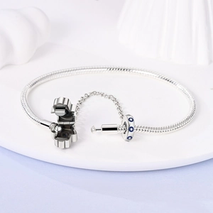 Detail of silver snake chain bracelet with evil eye charm and safety chain on white tray