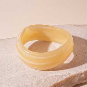 Close-up of a wide yellow acrylic bangle with sand texture on natural stone