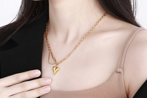Dettaglio della collana con pendente a cuore dorato indossata con catena asimmetrica
