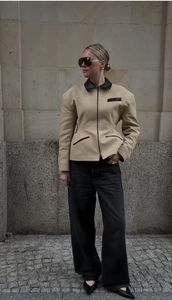 Detail of beige jacket with black lapels and zipper closure styled with wide leg jeans