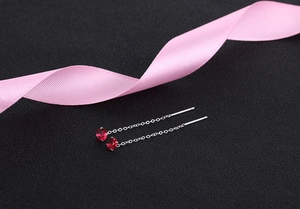 Macro shot of 925 silver threader earrings with red zircon on black texture background