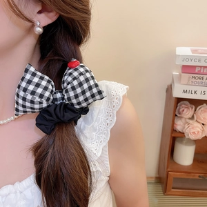 Detail of black and white checkered bow hair scrunchie with red heart accent on model