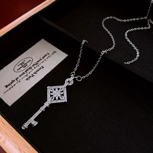 Detailed macro view of a silver key pendant with zircon flower head on black velvet