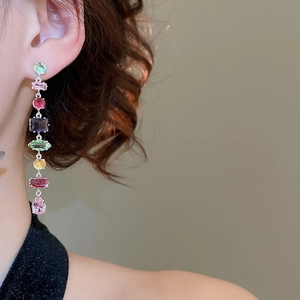 Close-up of dangling long tassel earrings with colorful square zircons on model